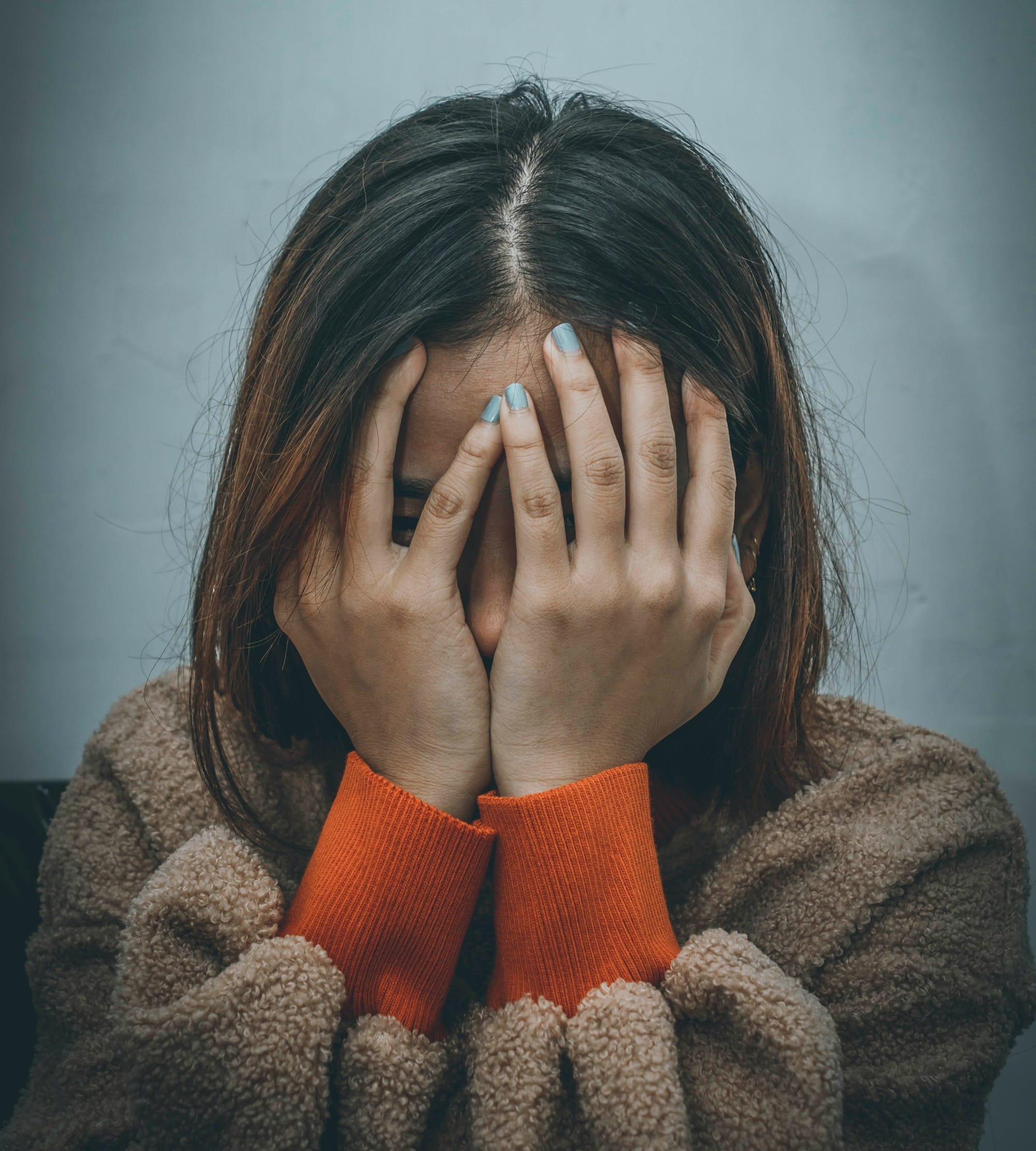 woman in brown sweater covering her face with her hand